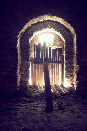 The arched entrance to old castle is closed by fences in middle and supported by board. The sun's rays break through cracks in the door boards.の写真素材
