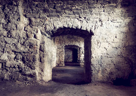 Basement tunnel of the old castle. The stone walls of the prison. A long corridor through several rooms. Earthen floor.の写真素材