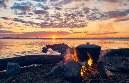 The cauldron with tea is boiled on the fire. Weekend on the river. Dawn by the water. Cooking over a campfire.の写真素材