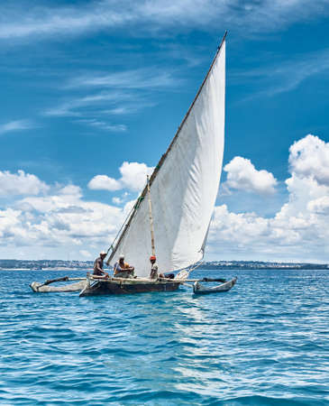 Zanzibar, Tanzania - 03.18.2021: Fishermen fishing on a white sailboat. Turquoise ocean on a background of cloudy African sky.の写真素材