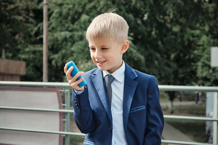 Schoolboy talking on the phone. Blond boy on the street during the day. Preparing for school. Break...