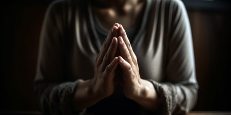 Close up of woman praying in the dark room with her hands togetherの素材