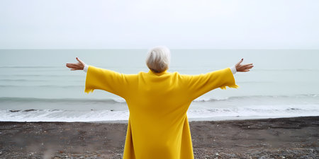 Elderly woman in yellow raincoat on the beach. Rear viewの素材