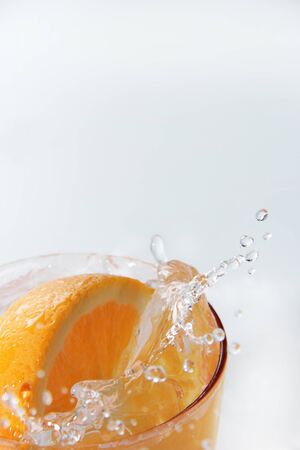 Splash from a slice of orange drop into a glass of water, On the white backgroundの写真素材