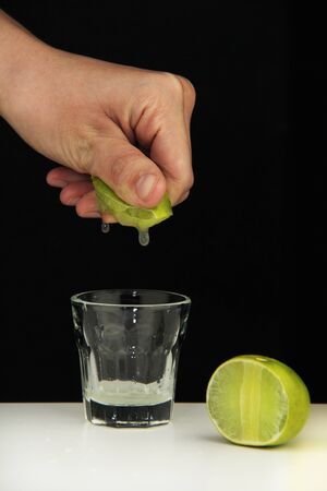 Hand squeeze lime with lime drop into glass on black backgroundの写真素材