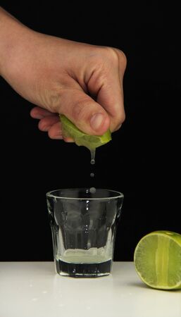 Hand squeeze lime with lime drop into glass on black backgroundの写真素材