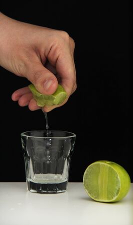 Hand squeeze lime with lime drop into glass on black backgroundの写真素材