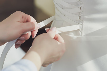 Close up of female hands ties the lacing of wedding dress. Preparation of the bride.の写真素材