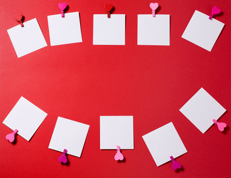 Six white paper sheets pinned with clothespin decorated with wooden hearts. Red background, copy space.の写真素材
