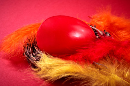Close Up of a big red egg in the nest with colored feathers on the red background. Easter greeting card.の写真素材