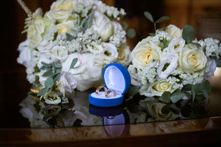 golden wedding rings in a blue gift box and a bridal bouquet made of white roses. close-up, macroの写真素材