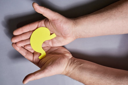 Yellow Paper Human Stomach Symbol in Human Hands on Gray Background. Close-upの写真素材