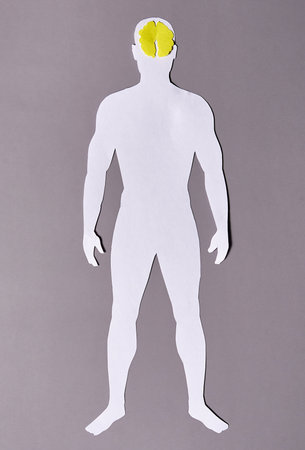 A paper silhouette of a man with a yellow brain on a gray background.の写真素材