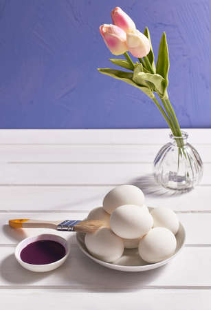 Easter card. Eggs, brush, paint, a bouquet of tulips on a white table on a lilac background. Copy spaceの写真素材
