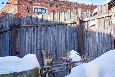 A wooden fence and a broken machine, covered in snow. Abandoned territory of an old factory.の写真素材