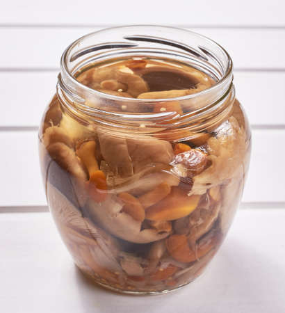 A jar of homemade pickled wild mushrooms on a white wooden table. Traditional Russian snack. Close-up, macroの写真素材
