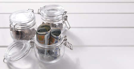 Glass jars with coins and cash on a white wooden background. Close-up, macro, copy space