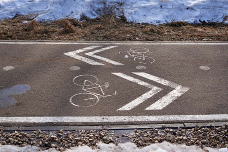 Bike path in the park against the background of melting snow in spring. White symbols on the...