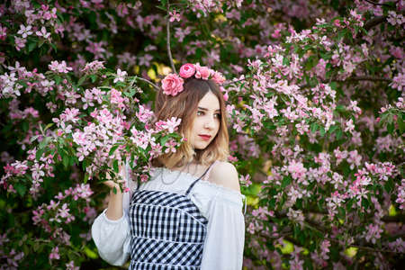 A young girl in a wreath of roses inhales the fragrance of a flowering tree. An idea for a photo shoot.の写真素材