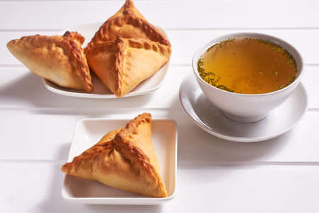 Traditional Tatar pastries "ochpochmak" on a white platter and chicken broth with dill in a white bowl on a white wooden background. Close-up.の写真素材
