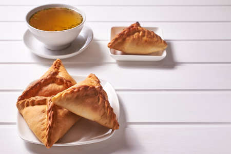 Traditional Tatar pastries "ochpochmak" on a white platter and chicken broth with dill in a white bowl on a white wooden background. Close-up with copy space.の写真素材