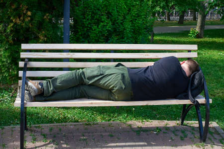 A tired tourist sleeps on a bench in the park, putting a backpack under his head. Close-upの写真素材