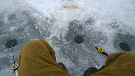 Winter fishing rods on the ice near fishing hole and fisherman's legs. Suitable for any purpose useの写真素材