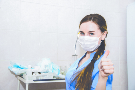 Female doctor woman in mask show thumb up hand sign with hospital backgroundの写真素材