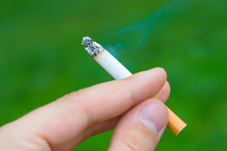 Cigarette in the hand with smoke on a green background isolatedの写真素材