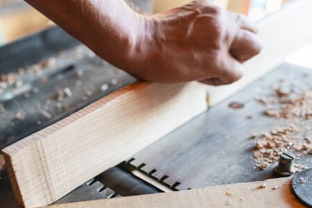 Woodworking machine process a wooden plank. Workers hand hold a wooden plank. Selective focus. Manual wood processing concept.の写真素材