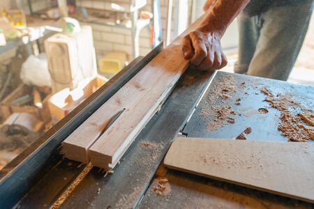 Woodworking machine process a wooden plank by a circular saw. Workers hands hold a wooden plank.  Manual wood processing concept.の写真素材