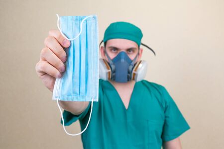 Medical mask in doctors hand in green suit on the smooth yellow background. Medical concept....