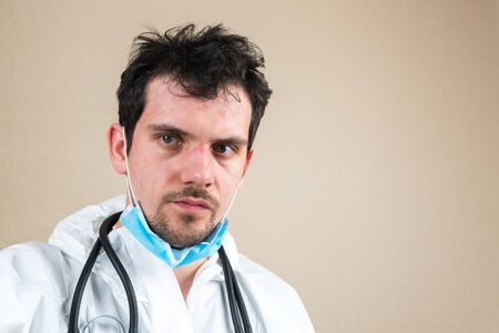 Male doctor wearing white protective suit mask and stethoscope with wounds from protective respirator after work day isolatedの写真素材