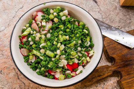 Salad with radish and onion in white metal plate on the table near wooden cutboard and knife, High quality photoの写真素材