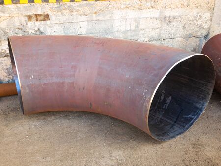 Withdrawal for industrial metal pipe at a right angle on the concrete floor. Curved rusty metal pipe of large diameter at an angle of 90 degrees. High quality photoの写真素材