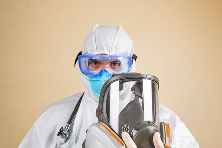 Doctor wearing white protective suit and stethoscope full face respiratory mask in hand isolated. Selective focus.の写真素材