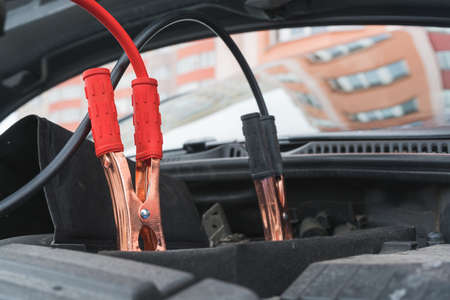 Jump cables on car low power battery. Black and red. Broken car start attempt. Selective focus.の写真素材