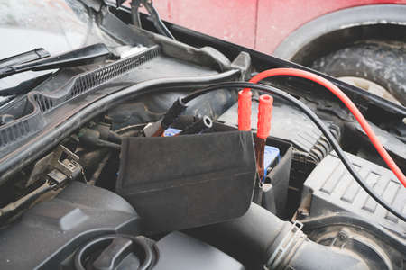 Jump cables on car low power battery. Black and red. Broken car start attempt at winter. Selective focus.の写真素材