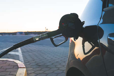 Red Petrol Pump Refueling Gun in the Tank of a Black Car close up