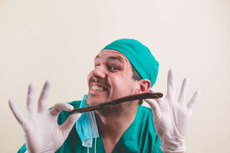 Young doctor in green surgeon suit and protective breathing mask with straight razor in hand isolated on the yellow backgroundの写真素材