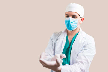 Young doctor in white suit and protective breathing mask puts gloves on his hands on yellow background isolated.の写真素材