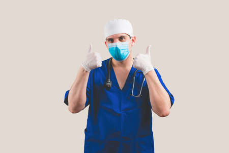 Young doctor with thumbs up in blue surgeon suit and glasses with stethoscope on the yellow background isolatedの写真素材