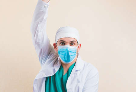 Shocked doctor in protective medical mask and white lab coat with handup close up isolated