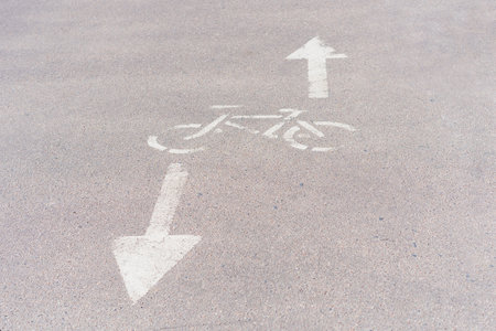 This photo features a detailed close-up of a bicycle sign painted on the asphalt pavement. The sign indicates a bicycle lane on the sidewalk and features a white silhouette of a bike with directional arrows. The pavement around the sign is worn and textured, with subtle cracks and imperfections. This image would be a great addition to any collection related to urban transportation, cycling, or street signageの写真素材