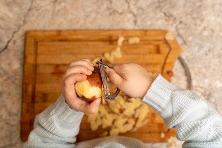Child's Hands Using a Metal Vegetable Peeler to Peel a Potato Over a Wooden Cutting Boardの写真素材