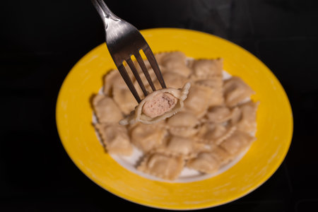 Homemade pelmeni on a yellow plate. A close-up shot highlighting the appetizing crimped edges and delicious filling, with one pelmeni on a fork.の写真素材