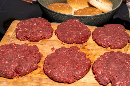Six raw ground beef patties neatly placed on a wooden cutting board. The coarse-textured patties are fresh and ready for grilling or frying, capturing the essence of burger preparation.の写真素材