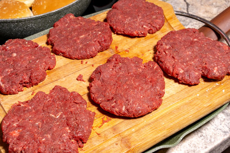 Six raw ground beef patties neatly placed on a wooden cutting board. The coarse-textured patties are fresh and ready for grilling or frying, capturing the essence of burger preparation.の写真素材