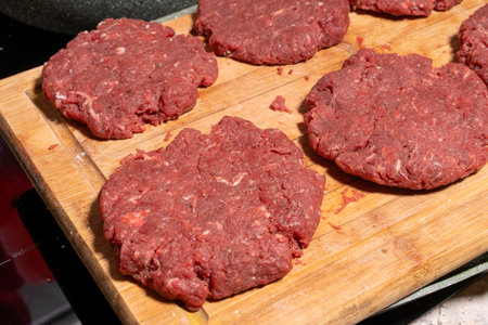 Six raw ground beef patties neatly placed on a wooden cutting board. The coarse-textured patties are fresh and ready for grilling or frying, capturing the essence of burger preparation.の写真素材