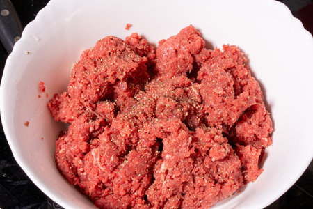 A white scalloped bowl filled with seasoned raw ground meat. The coarse red meat is speckled with visible spices, making it ideal for preparing burgers, meatballs, or patties.の写真素材